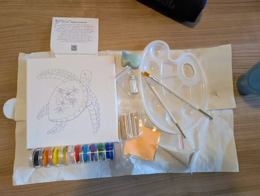 Artistic supplies including a turtle drawing, paint palette, brushes, and colour swatches on a wooden surface.